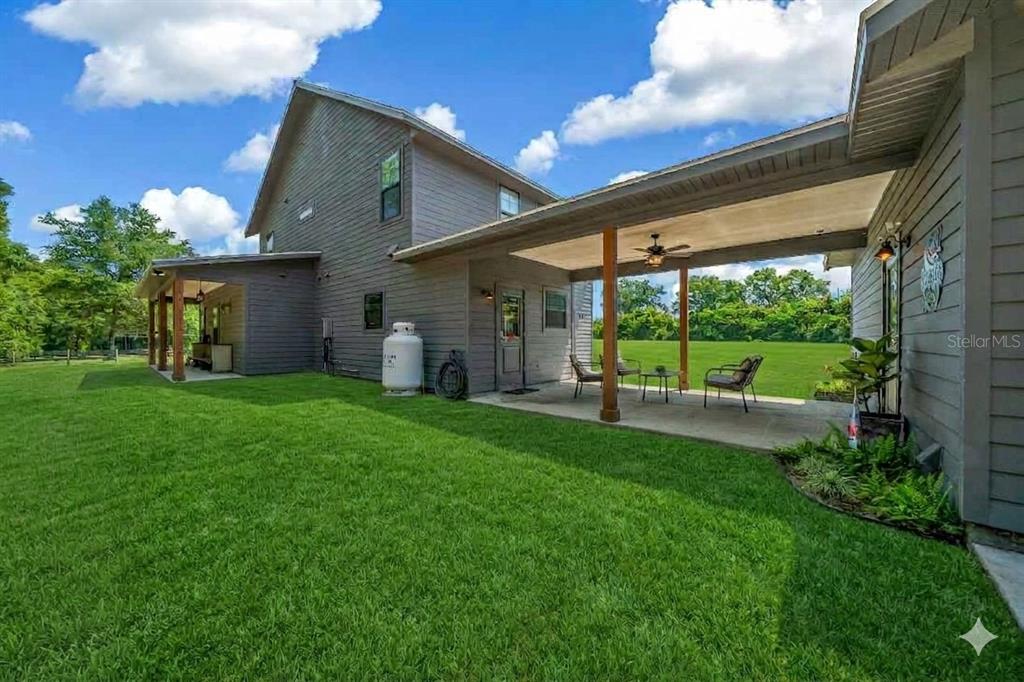 A gray two-story house features a covered patio with a ceiling fan and lawn — 13576 NW COUNTY ROAD 235, ALACHUA, FL