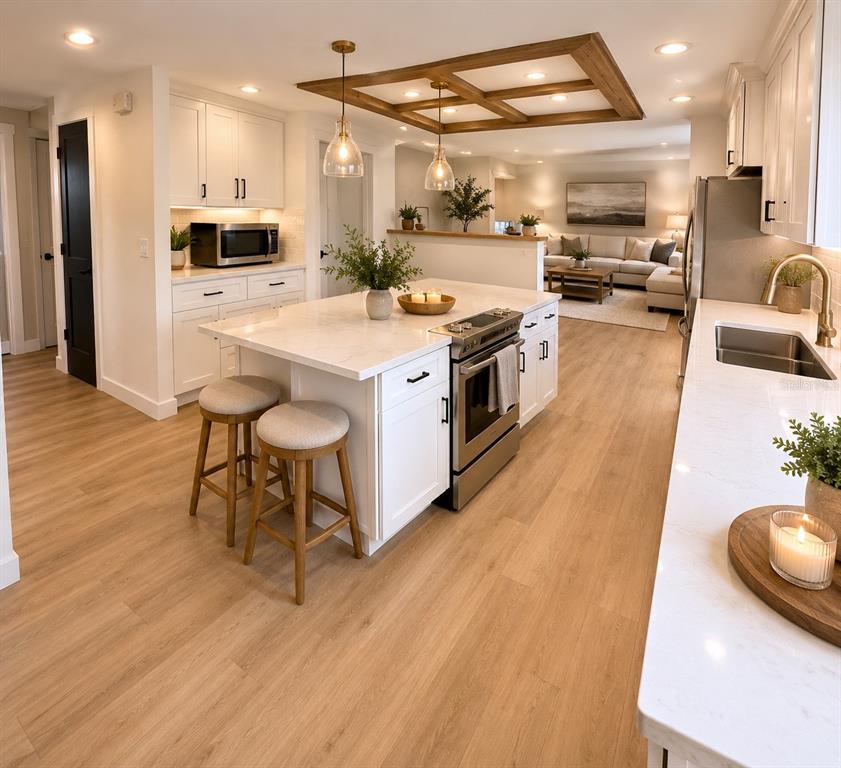 A modern kitchen features a white island with a range, light wood flooring, and pendant lighting — 6805 22ND AVENUE W, BRADENTON, FL