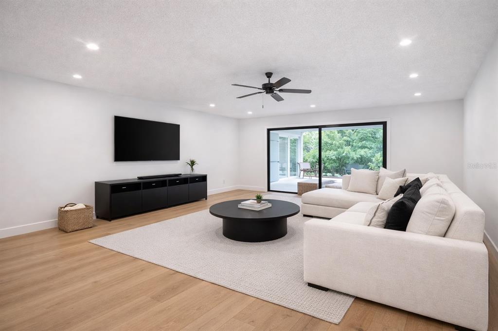 A living room with light wood floors, a white sectional sofa, and a black media console — 6805 22ND AVENUE W, BRADENTON, FL
