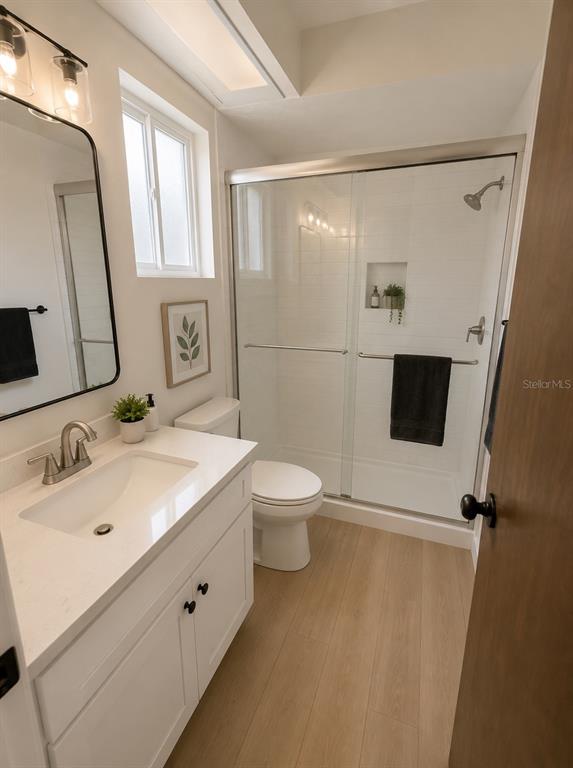 A bathroom features a white vanity, a glass-enclosed shower, and light wood-look flooring — 6805 22ND AVENUE W, BRADENTON, FL
