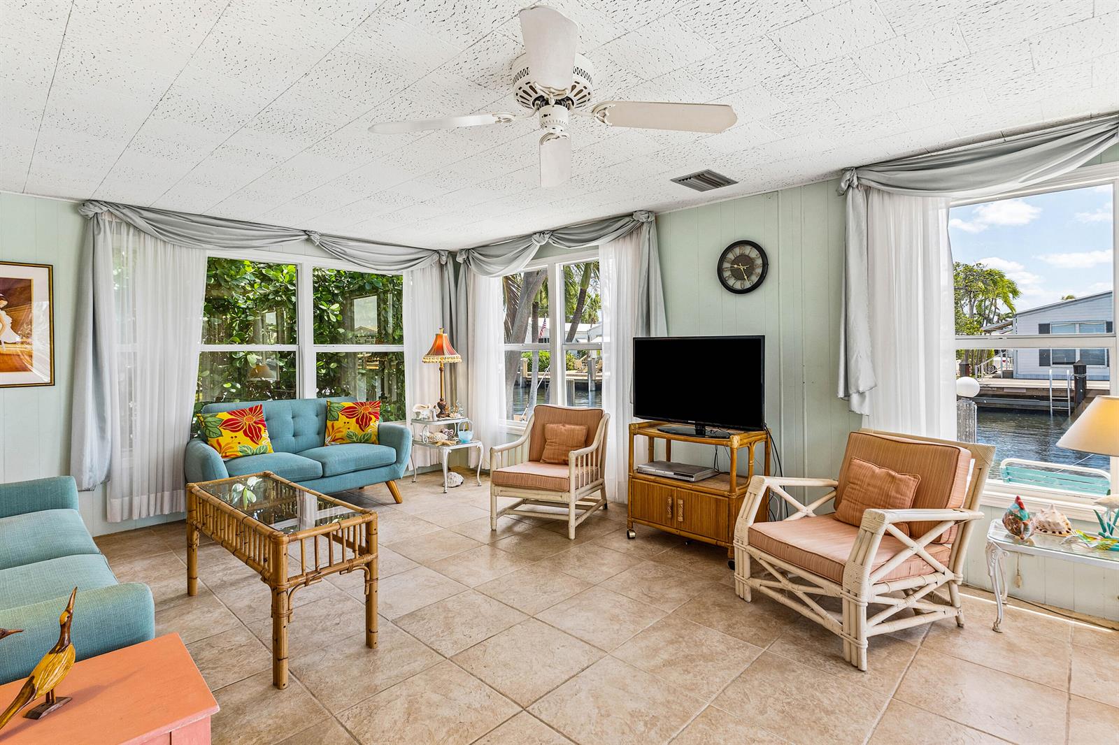 A sunroom features tile floors, wicker furniture, a ceiling fan, and views of a canal — 205 S Ibis Drive # R, Briny Breezes FL 33435, BRINY BREEZES, FL
