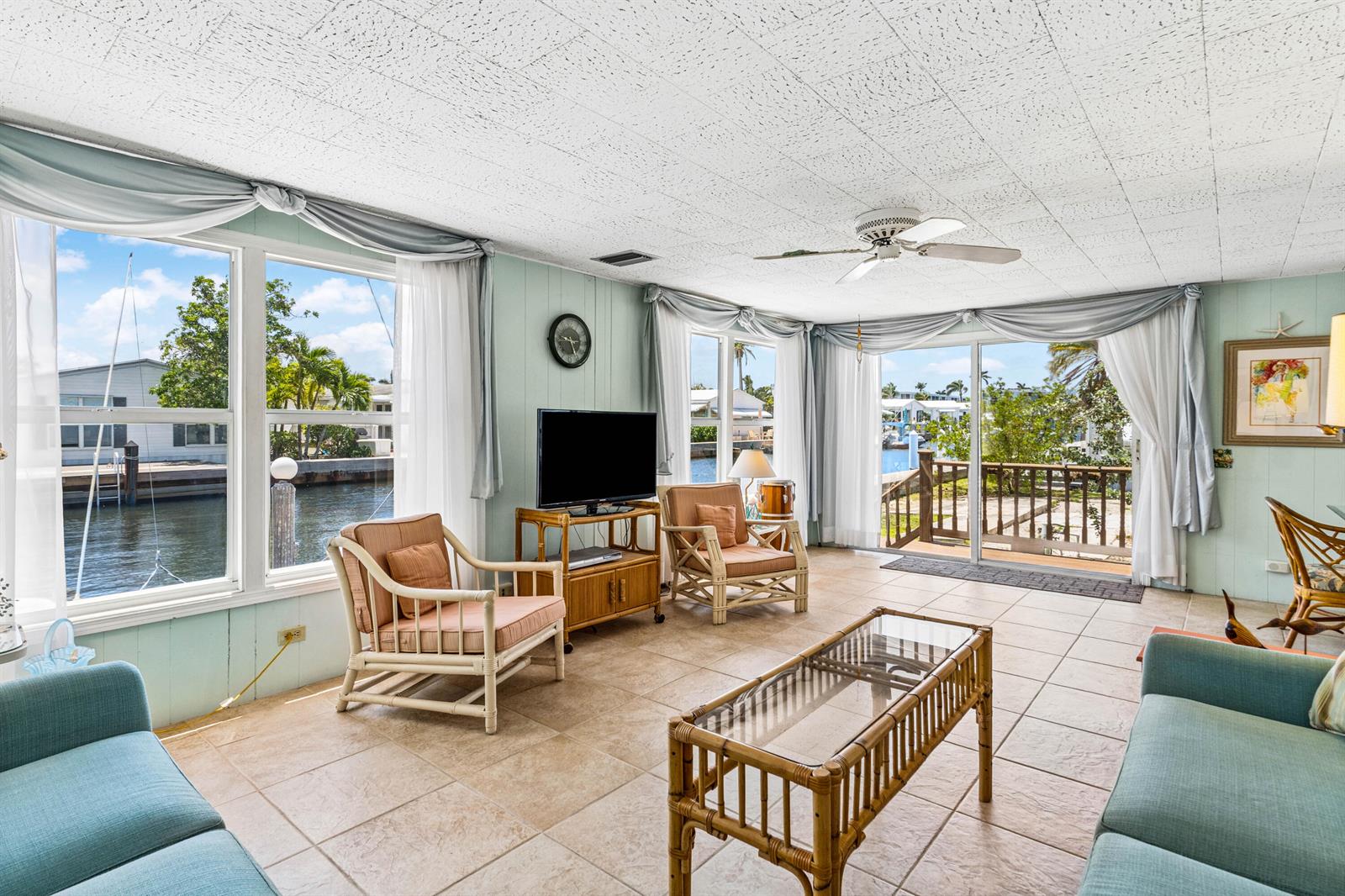 A sunlit living room features tile floors, wicker furniture, and large windows overlooking a canal — 205 S Ibis Drive # R, Briny Breezes FL 33435, BRINY BREEZES, FL