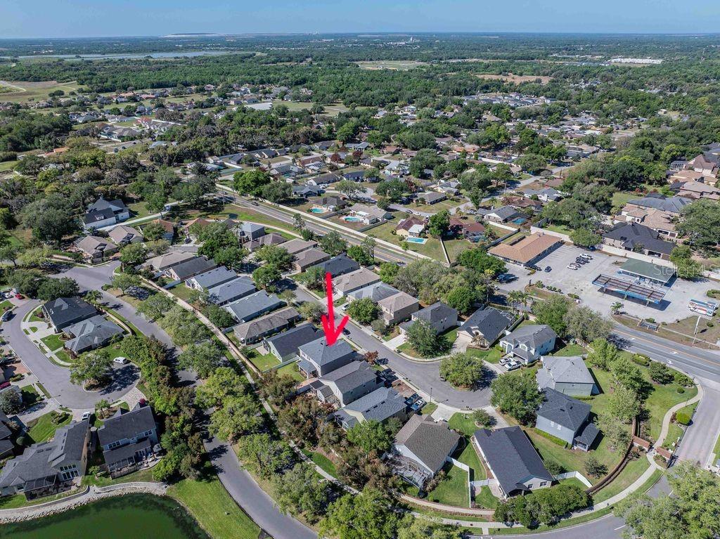 An aerial view shows a suburban neighborhood with a red arrow pointing to a house — 7018 CASCADES COURT, LAKELAND, FL