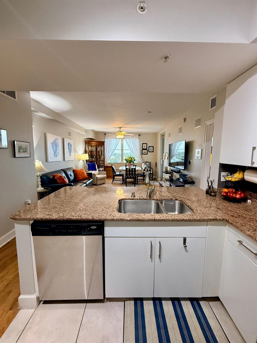 A kitchen with granite countertops and a stainless steel dishwasher overlooks an open living area — 1830 Radius Drive # 507, Hollywood FL 33020, HOLLYWOOD, FL
