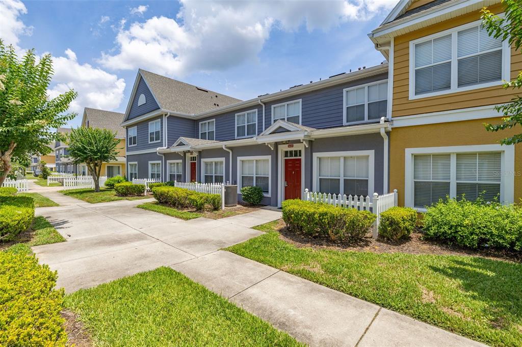 A multi-story townhouse complex with gray and yellow siding, red doors, and concrete walkways — 2620 LODI CIRCLE UNIT 103, KISSIMMEE, FL