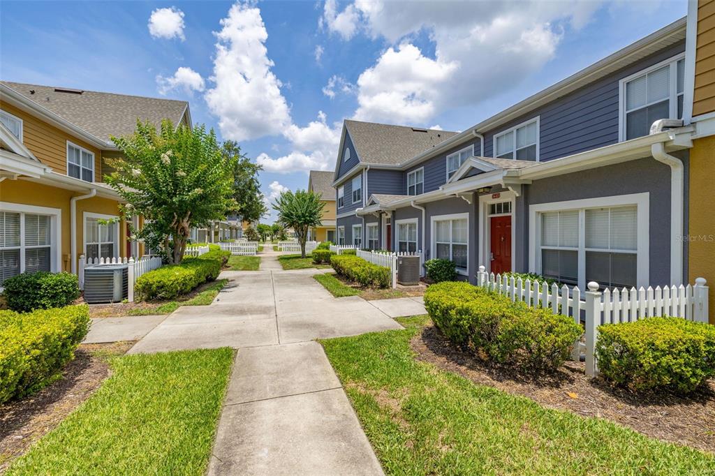 A sidewalk leads between two rows of multi-story townhomes with small front yards and fences — 2620 LODI CIRCLE UNIT 103, KISSIMMEE, FL