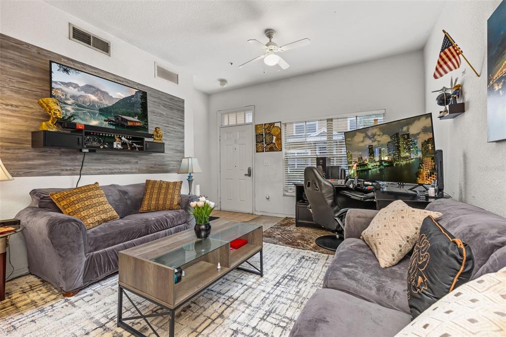 A living room features two gray sofas, a coffee table, and a desk with monitors — 2620 LODI CIRCLE UNIT 103, KISSIMMEE, FL