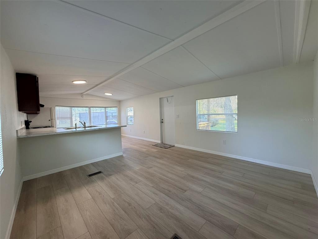 An open-concept living area features light wood-look flooring, white walls, and a kitchen peninsula — 6811 ROCHELLE AVENUE UNIT 6, NEW PORT RICHEY, FL