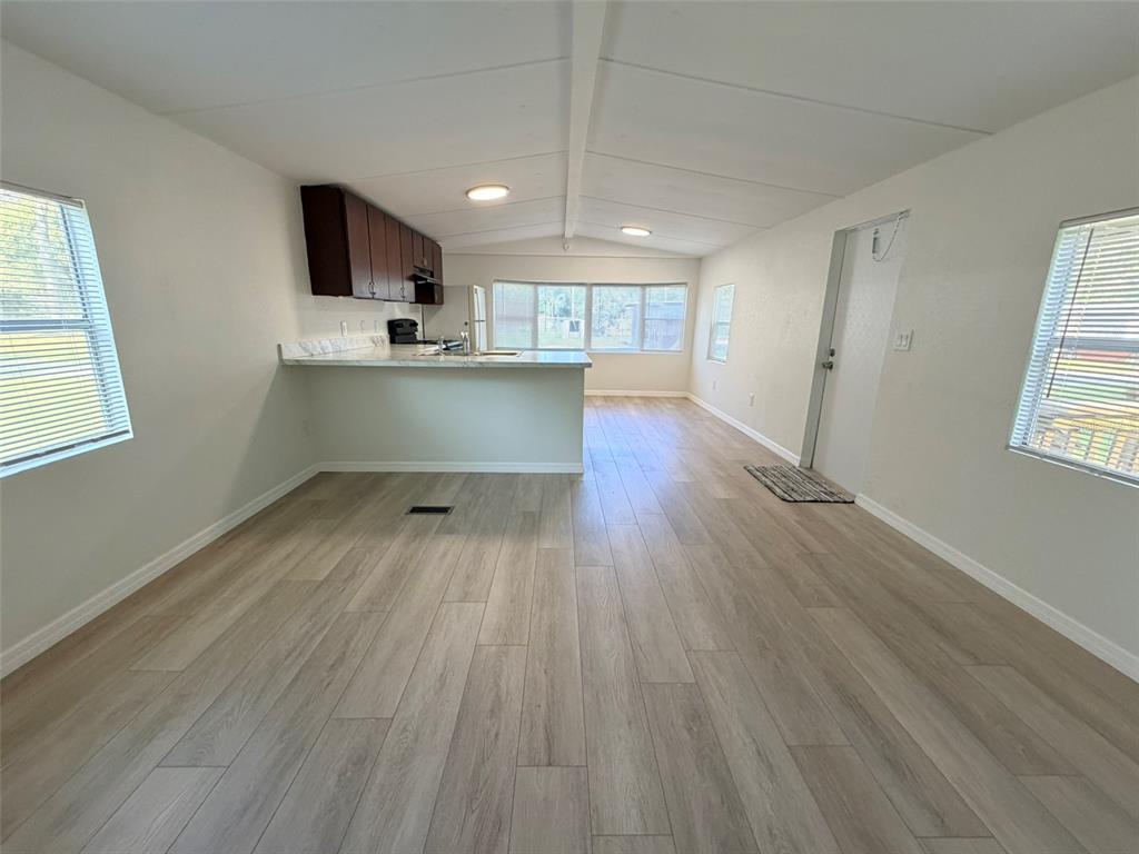 An open-concept living area features light wood-look flooring, white walls, and a kitchen with cabinets — 6811 ROCHELLE AVENUE UNIT 6, NEW PORT RICHEY, FL