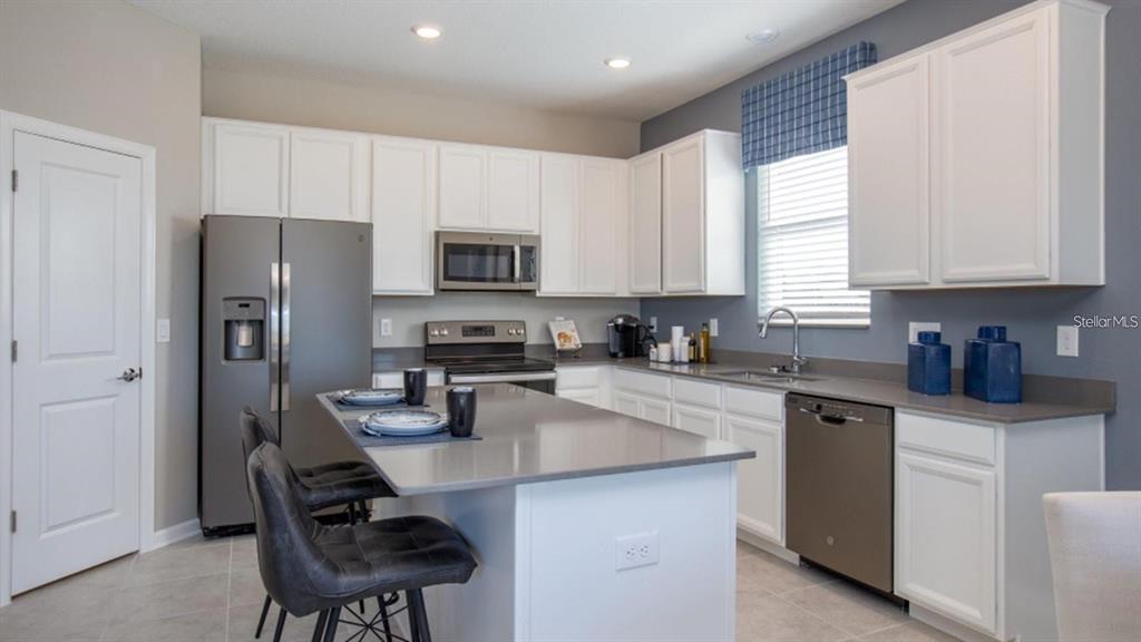 A modern kitchen features white cabinets, gray countertops, stainless steel appliances, and a central island — 643 GROVE STREET, WINTER HAVEN, FL