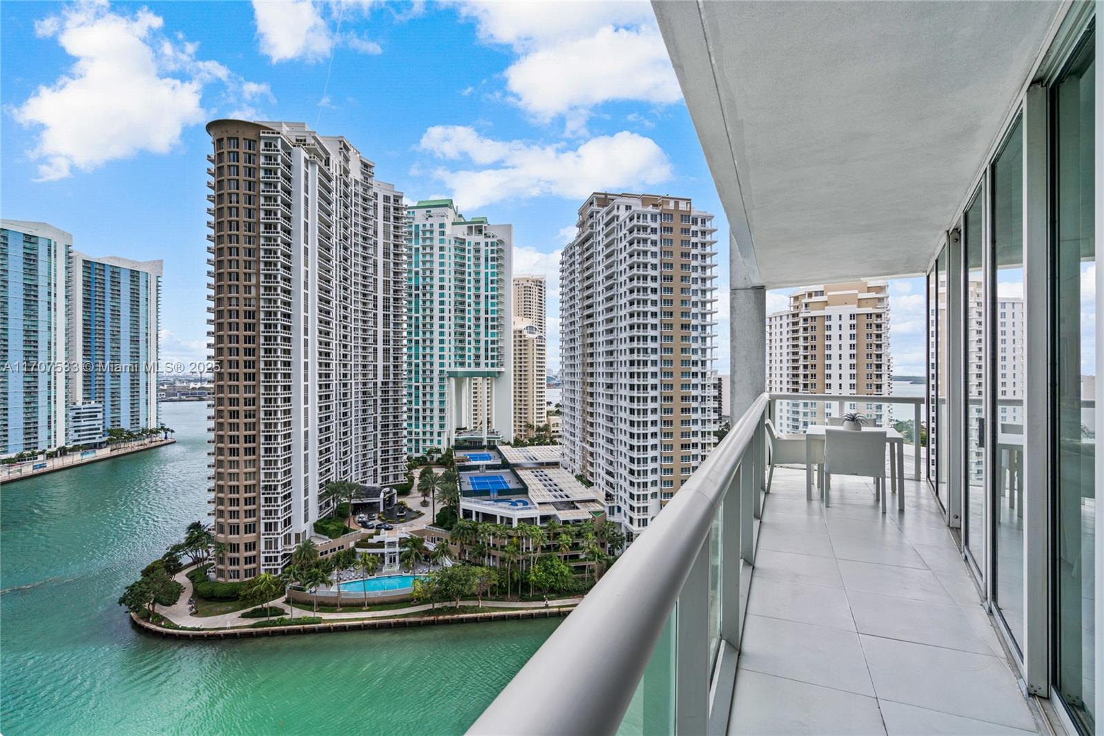 A balcony with a table and chairs overlooks a waterfront complex of high-rise buildings — 495 Brickell Ave # 1702, Miami FL 33131, MIAMI, FL