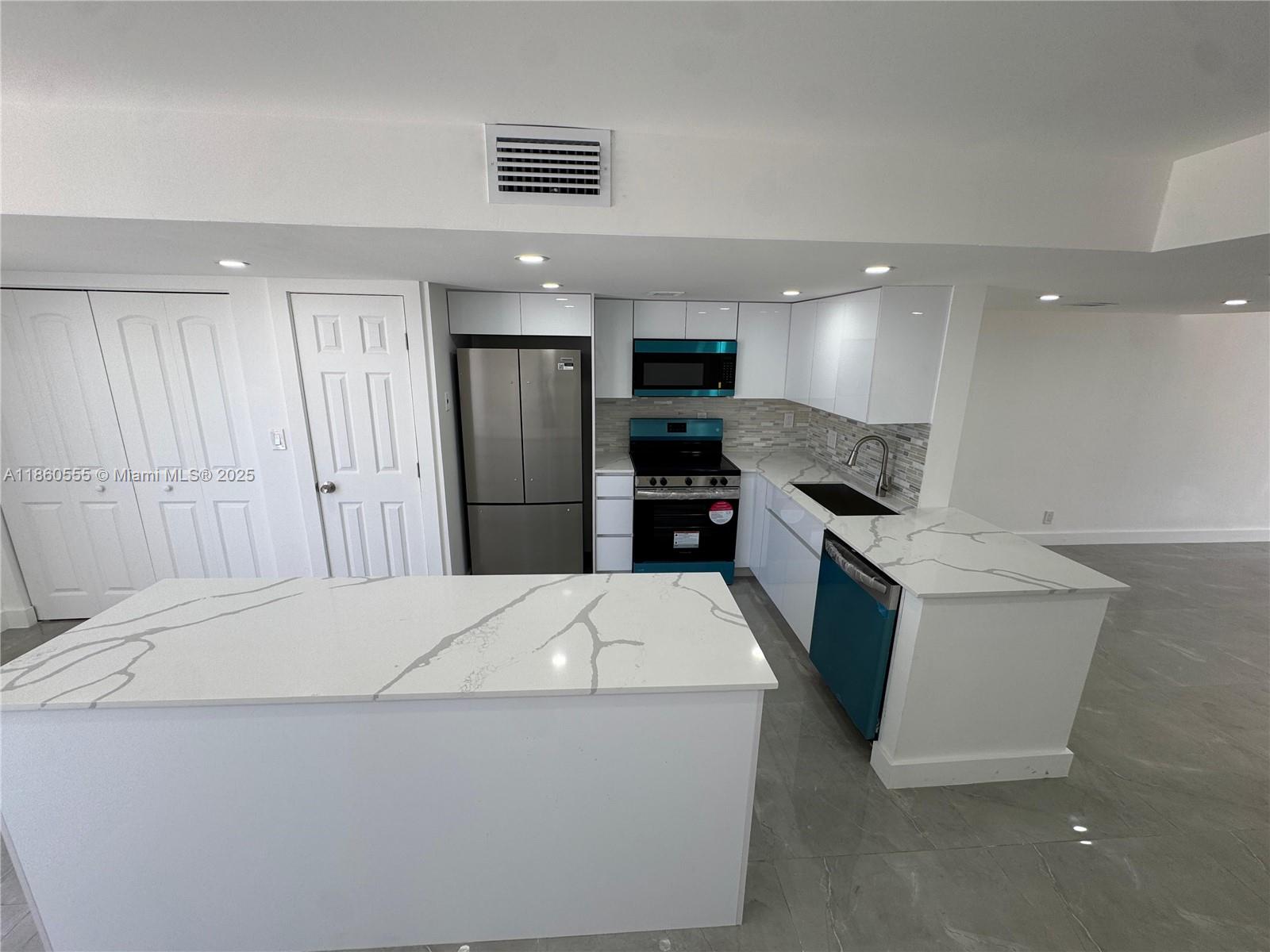 A modern kitchen features white cabinets, marble-patterned countertops, stainless steel appliances, and gray tile flooring — 2318 NE 7th St # 34, Hallandale Beach FL 33009, HALLANDALE BEACH, FL