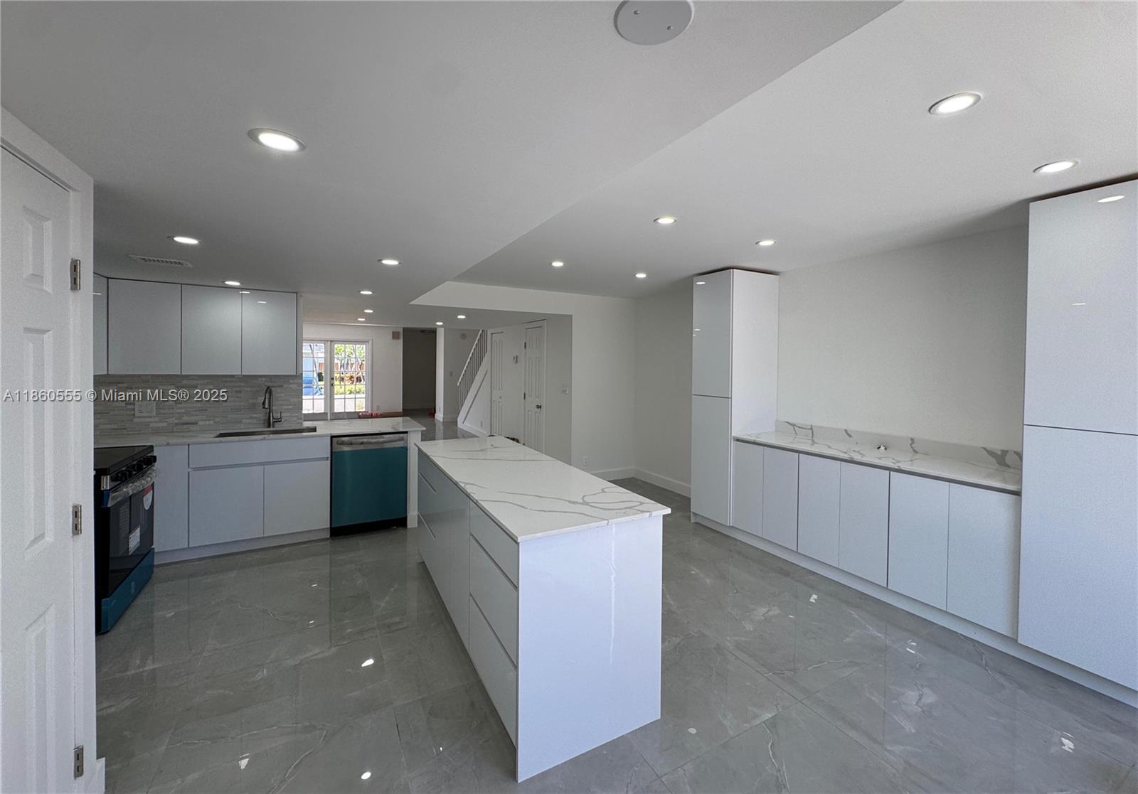 A modern kitchen features white cabinetry, a marble-topped island, and gray tile flooring — 2318 NE 7th St # 34, Hallandale Beach FL 33009, HALLANDALE BEACH, FL