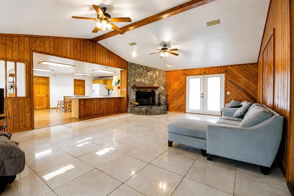 A spacious living room with tile floors, wood-paneled walls, a stone fireplace, and ceiling fans — 128 NE 326TH AVENUE, CROSS CITY, FL