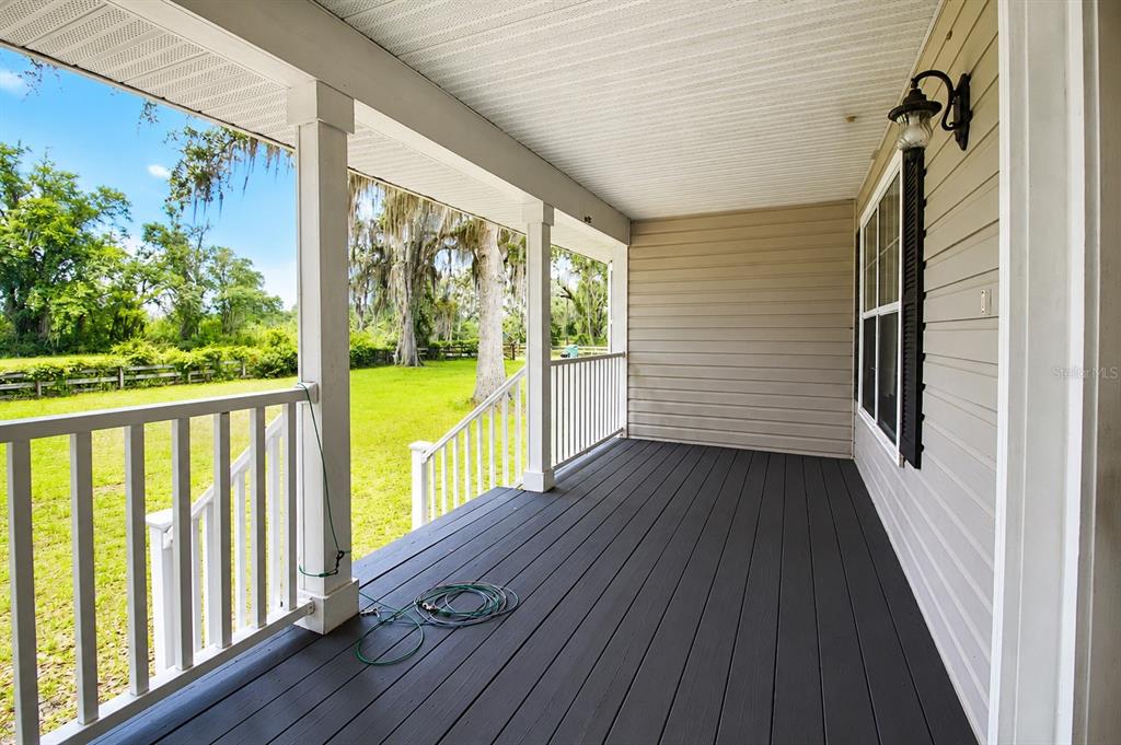 A covered porch with dark wood decking, white railings, and a view of a grassy yard — 128 NE 326TH AVENUE, CROSS CITY, FL
