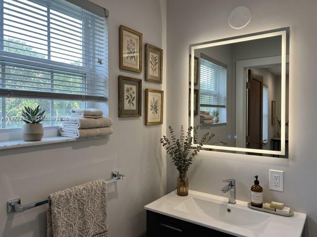 A bathroom features a vanity with a lighted mirror, a window with blinds, and framed art — 1500 NE 137th St, North Miami FL 33161, NORTH MIAMI, FL