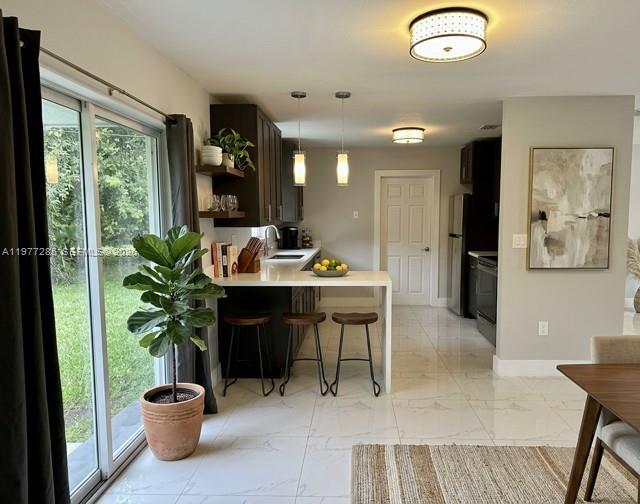 A modern kitchen features dark cabinetry, a white breakfast bar with stools, and tile flooring — 1500 NE 137th St, North Miami FL 33161, NORTH MIAMI, FL