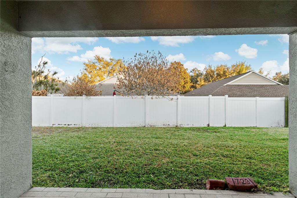 A view of a grassy backyard from a covered patio with a white vinyl fence — 723 ERIK LAKE ROAD, BRANDON, FL