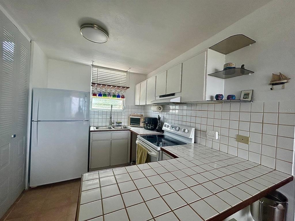 A kitchen features white cabinets, a tiled countertop, a white refrigerator, and a window — 5015 PUNTA TUNA UNIT 309, MAUNABO, PR