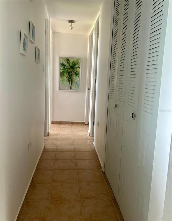 A hallway with tan tile flooring, white walls, louvered closet doors, and framed wall art — 5015 PUNTA TUNA UNIT 309, MAUNABO, PR