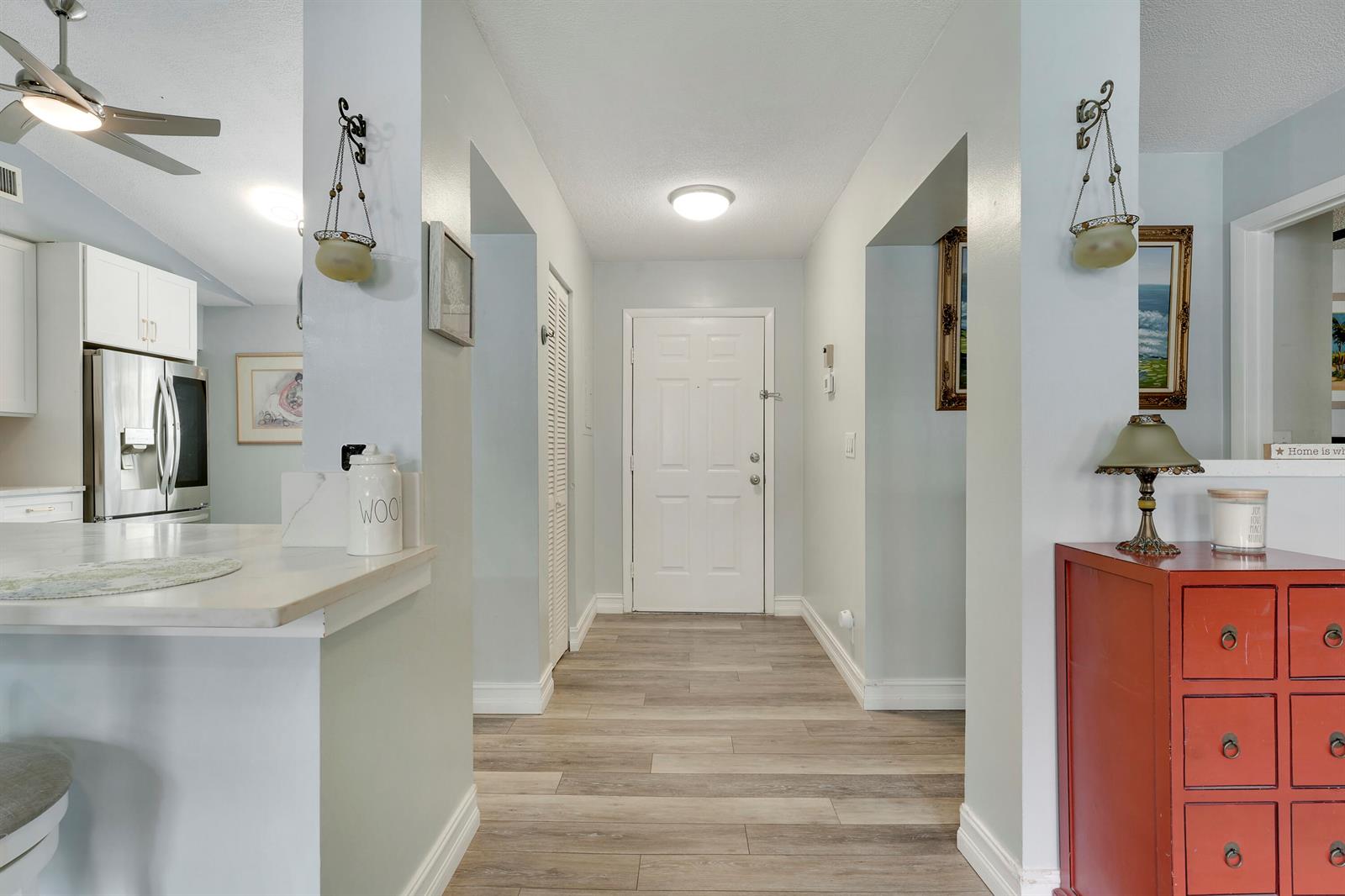 A hallway with wood-look flooring leads to a white front door between two wall openings — 3263 Perimeter Drive, FL 33467, FL