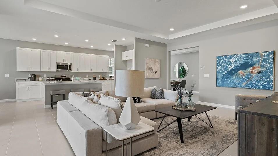 An open-concept living room features a white sectional sofa, a coffee table, and a kitchen — 1801 RIDER RAIN LANE, APOPKA, FL