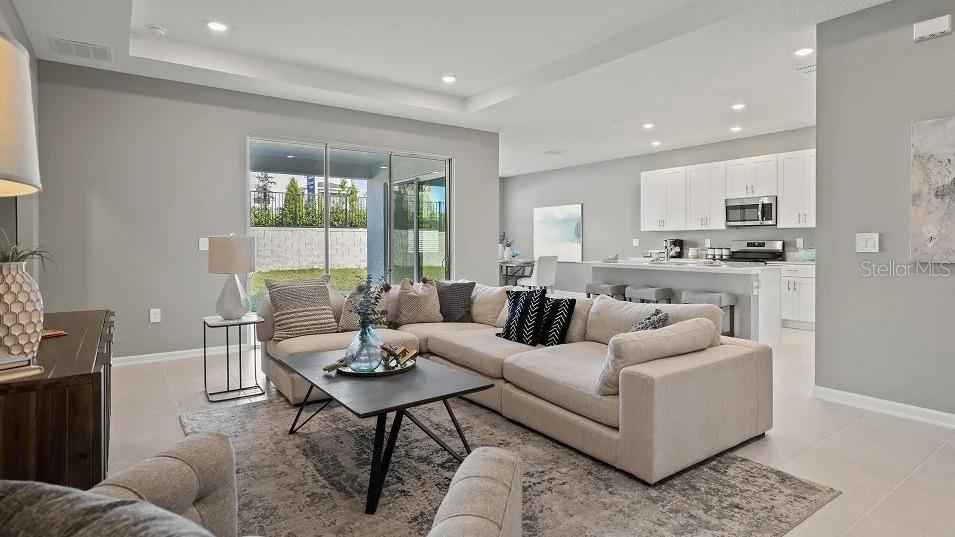 An open-concept living room with a sectional sofa, coffee table, and adjacent kitchen with island — 1801 RIDER RAIN LANE, APOPKA, FL