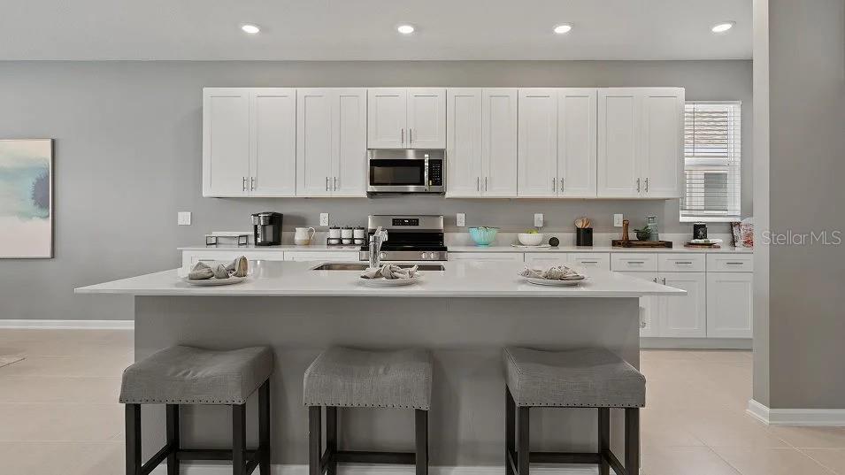 A modern kitchen features white cabinetry, a large quartz island, and three gray bar stools — 1801 RIDER RAIN LANE, APOPKA, FL