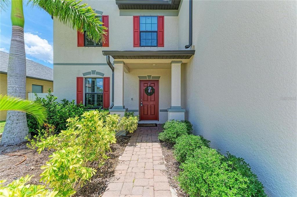 A brick walkway leads to the red front door of a two-story stucco house — 2084 LA PALMA AVENUE, PORT CHARLOTTE, FL