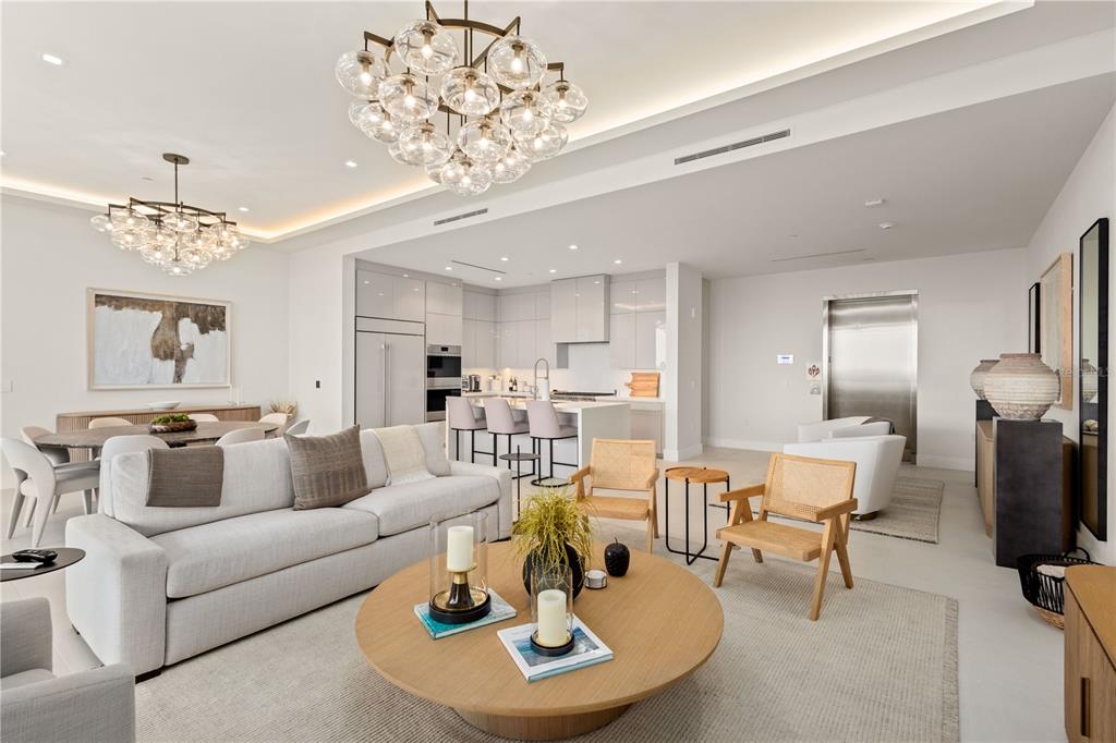 A modern open-concept living room features a large round coffee table, sofa, and kitchen island — 1581 GULF OF MEXICO DRIVE UNIT 507, LONGBOAT KEY, FL
