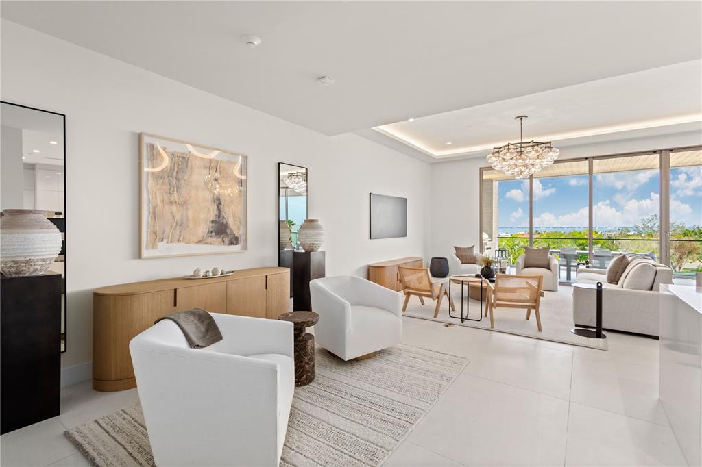 A bright, modern living room features white armchairs, a wooden sideboard, and floor-to-ceiling windows — 1581 GULF OF MEXICO DRIVE UNIT 507, LONGBOAT KEY, FL