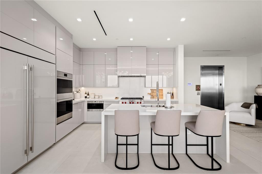 A modern kitchen features glossy light gray cabinetry, a white island, and three bar stools — 1581 GULF OF MEXICO DRIVE UNIT 507, LONGBOAT KEY, FL