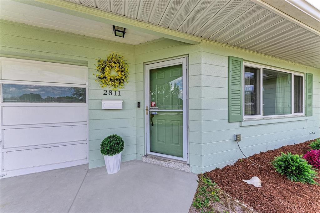 The exterior of a light green house features a front door, a window, and landscaping — 2811 33RD AVENUE W, BRADENTON, FL