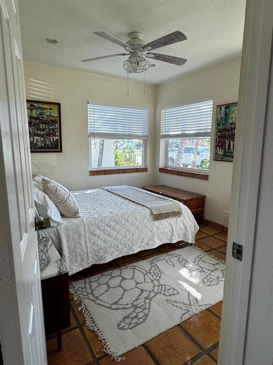 A bedroom features a bed, a turtle-patterned rug, tile flooring, and two windows with blinds — 256 E 24th Street, Riviera Beach FL 33404, RIVIERA BEACH, FL