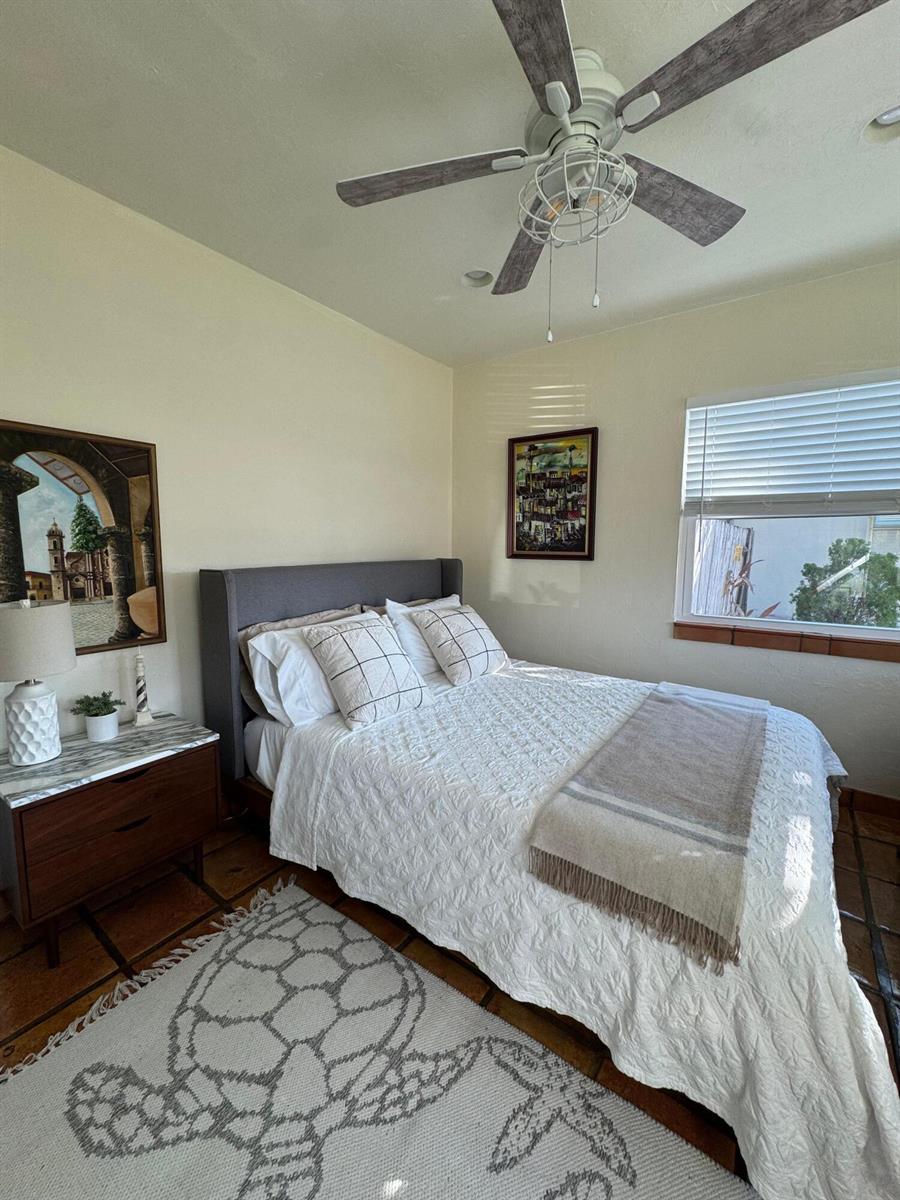 A bedroom features a gray upholstered bed, a wooden nightstand, and a ceiling fan — 256 E 24th Street, Riviera Beach FL 33404, RIVIERA BEACH, FL