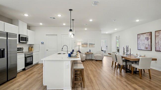 A modern open-concept kitchen and dining area with white cabinetry, a central island, and wood flooring — 31527 WILD GRAPE LANE, BROOKSVILLE, FL