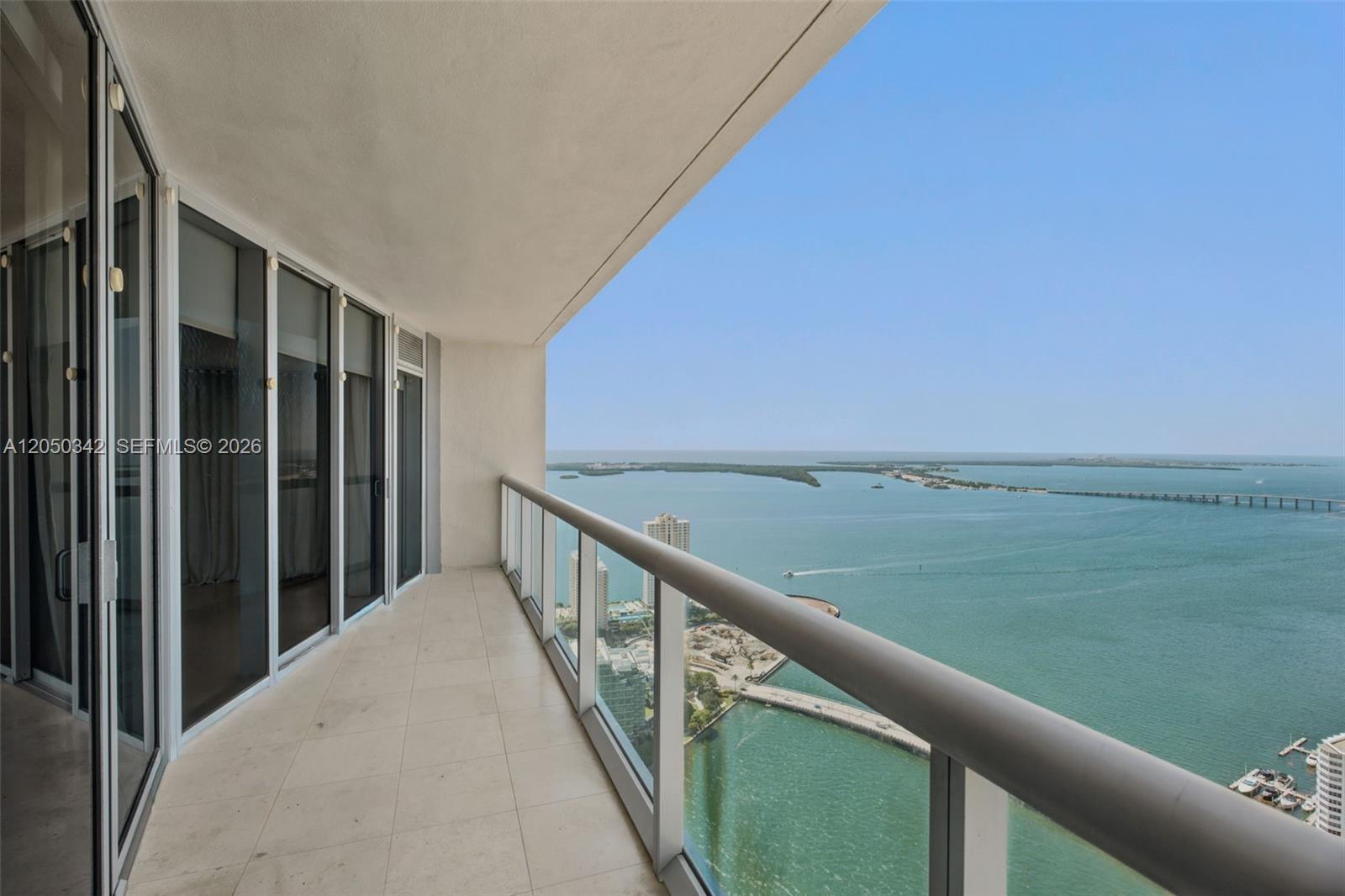 A high-rise balcony features glass railings overlooking a bay with a bridge and distant land — 495 Brickell Ave # 5309, Miami FL 33131, MIAMI, FL