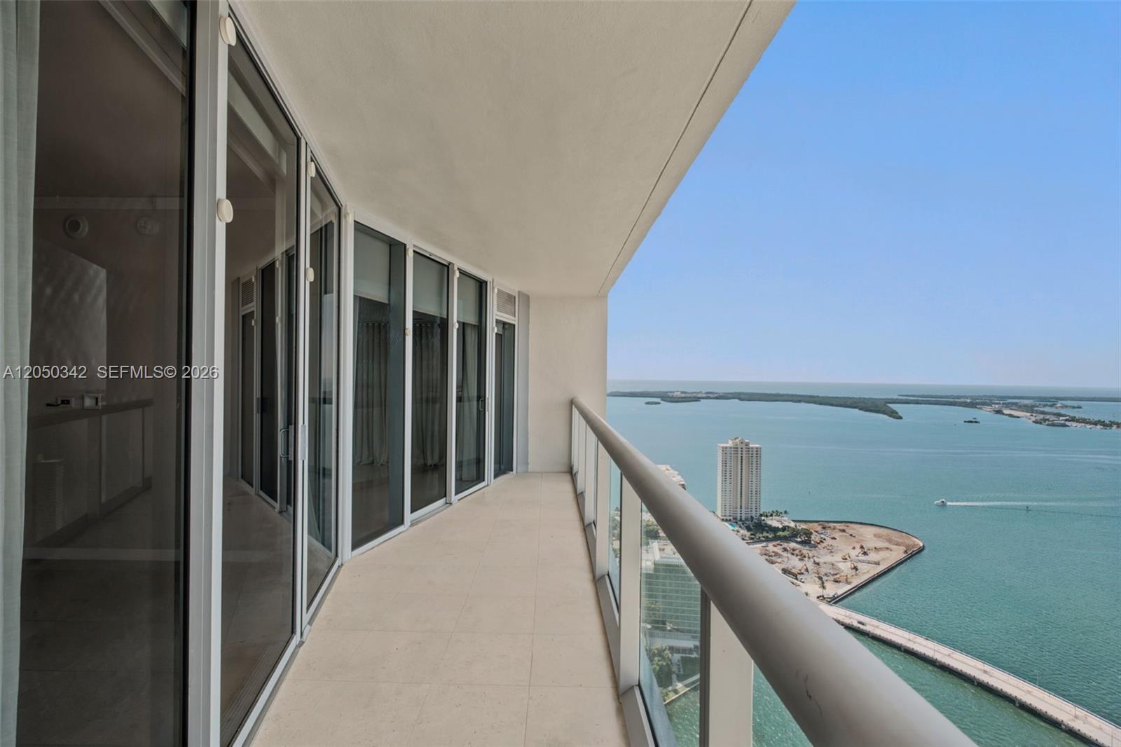 A high-rise balcony with glass railings overlooks a bay, a construction site, and distant islands — 495 Brickell Ave # 5309, Miami FL 33131, MIAMI, FL