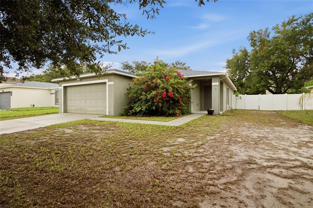 A single-story house with a garage, a large flowering bush, and a sandy front yard — 13708 TRAMORE DRIVE, ODESSA, FL