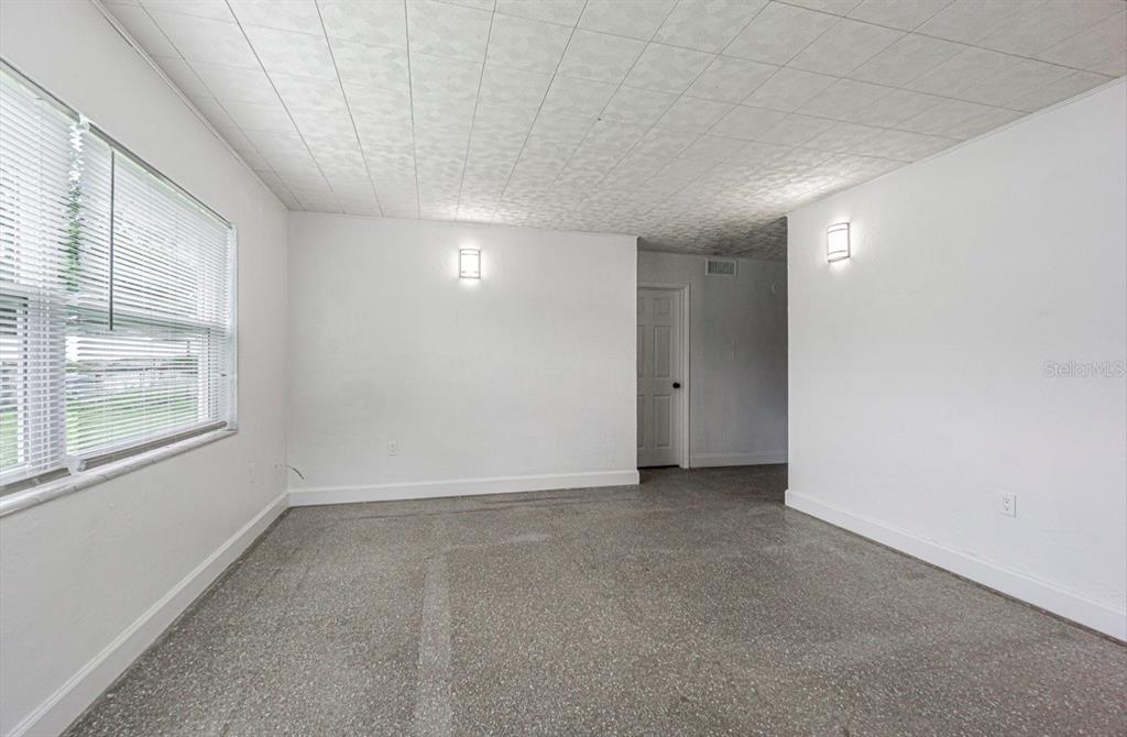 An empty room features white walls, a textured ceiling, two wall sconces, and speckled flooring — 8706 RUTH PLACE, TAMPA, FL