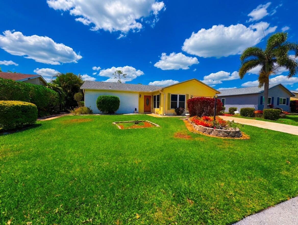 A yellow single-story house with a green lawn and a palm tree under a blue sky — 6304 Emerald Sky Lane, FL 33463, FL