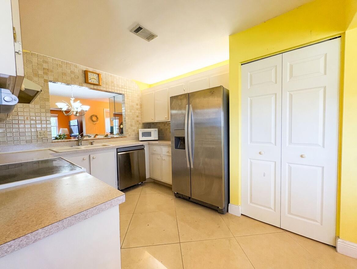 A kitchen with yellow walls, white cabinets, stainless steel appliances, and a tiled backsplash — 6304 Emerald Sky Lane, FL 33463, FL
