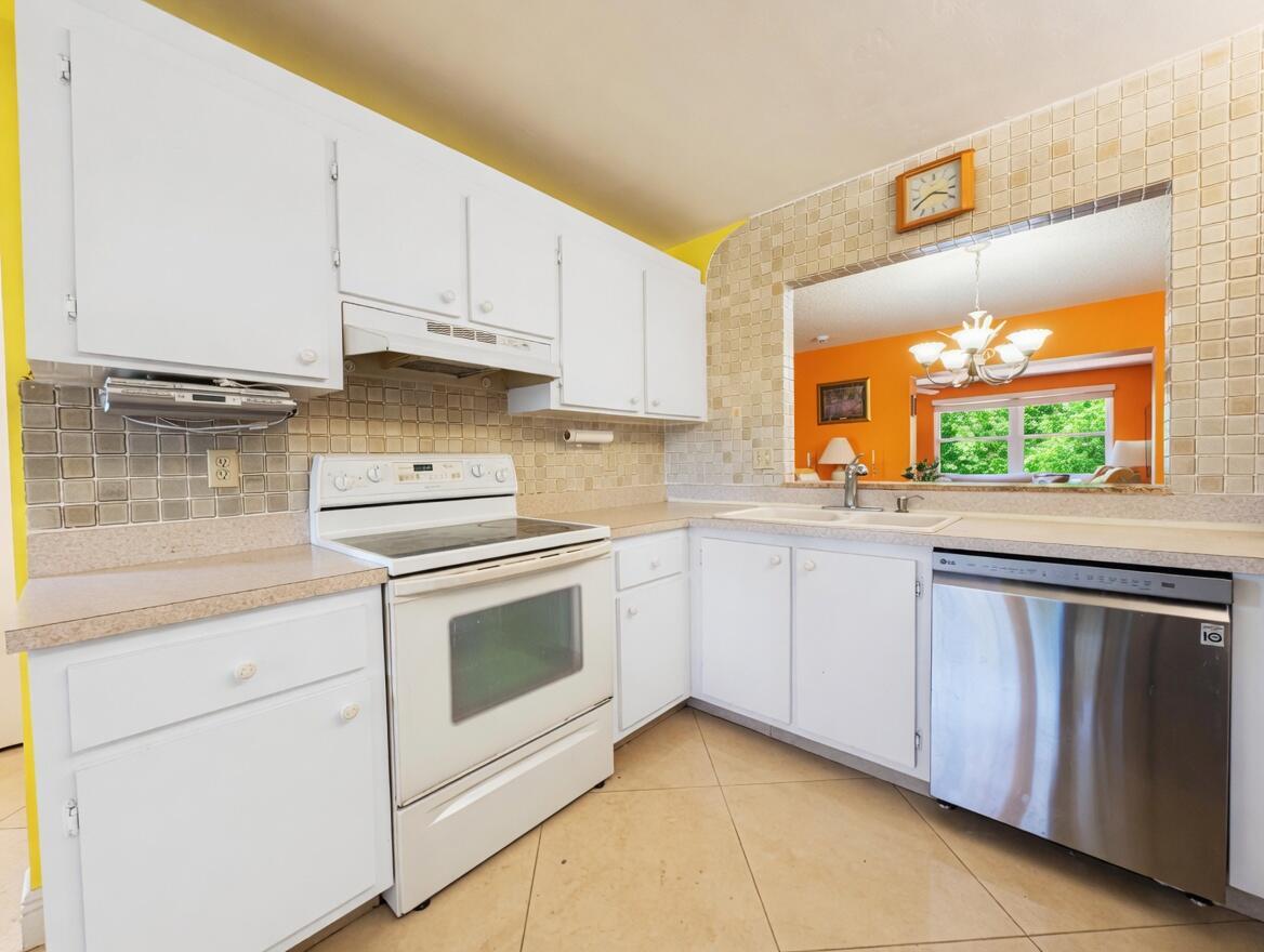 A kitchen with white cabinets, stainless steel dishwasher, white stove, and light-colored tile backsplash — 6304 Emerald Sky Lane, FL 33463, FL