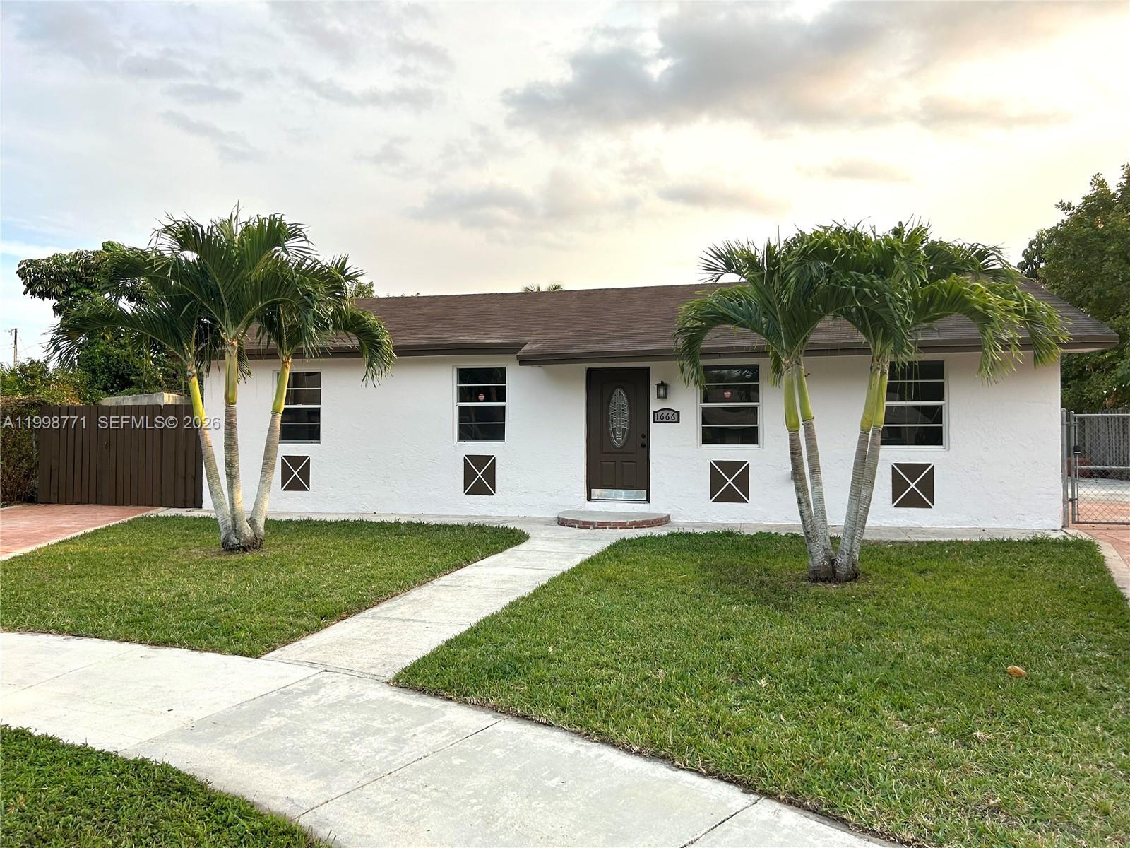A white single-story house features a brown front door, two palm trees, and a walkway — 1666 SW 3rd Ct, Homestead FL 33030, HOMESTEAD, FL