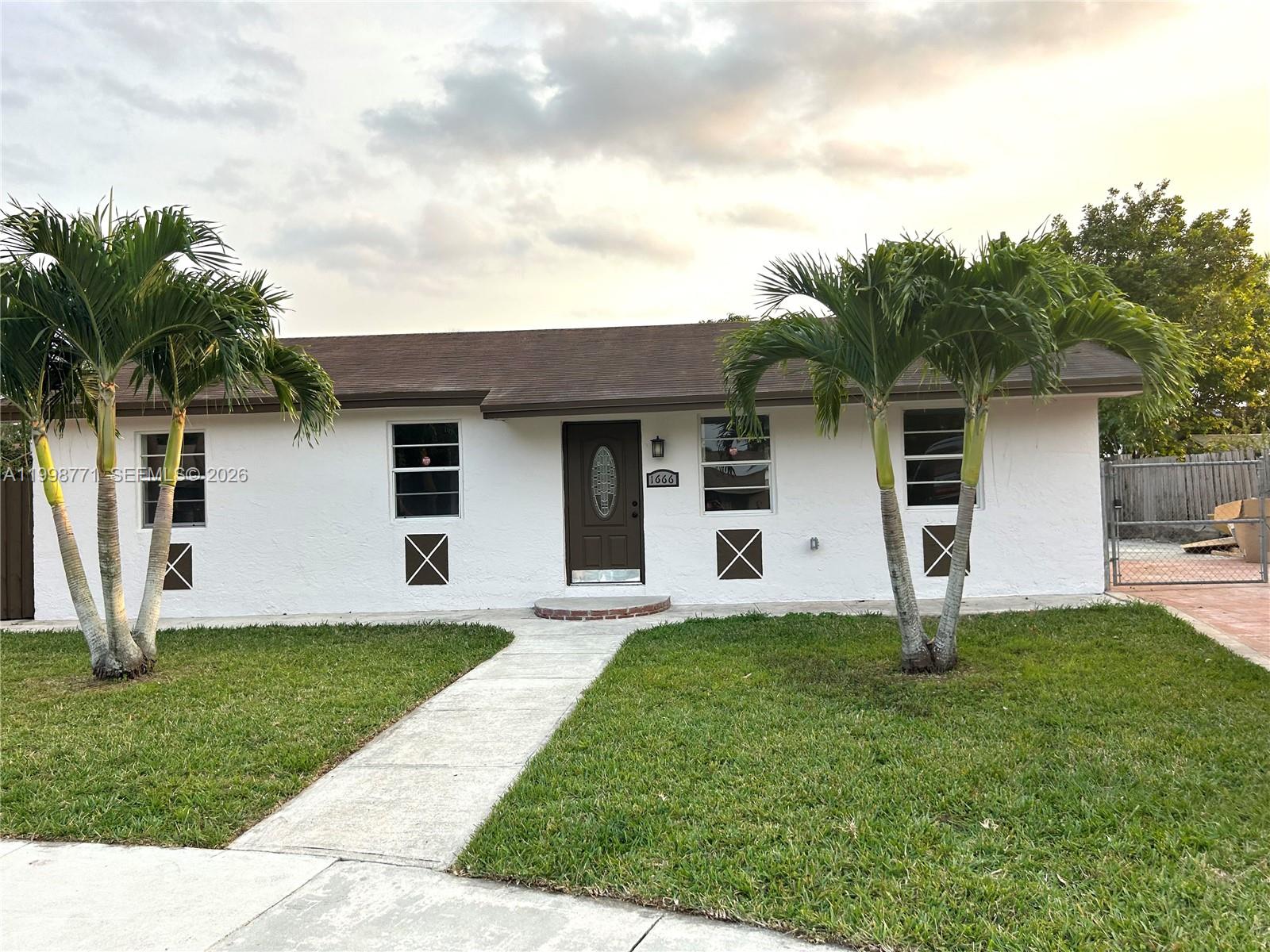 A single-story white house features a brown front door, two palm trees, and a walkway — 1666 SW 3rd Ct, Homestead FL 33030, HOMESTEAD, FL