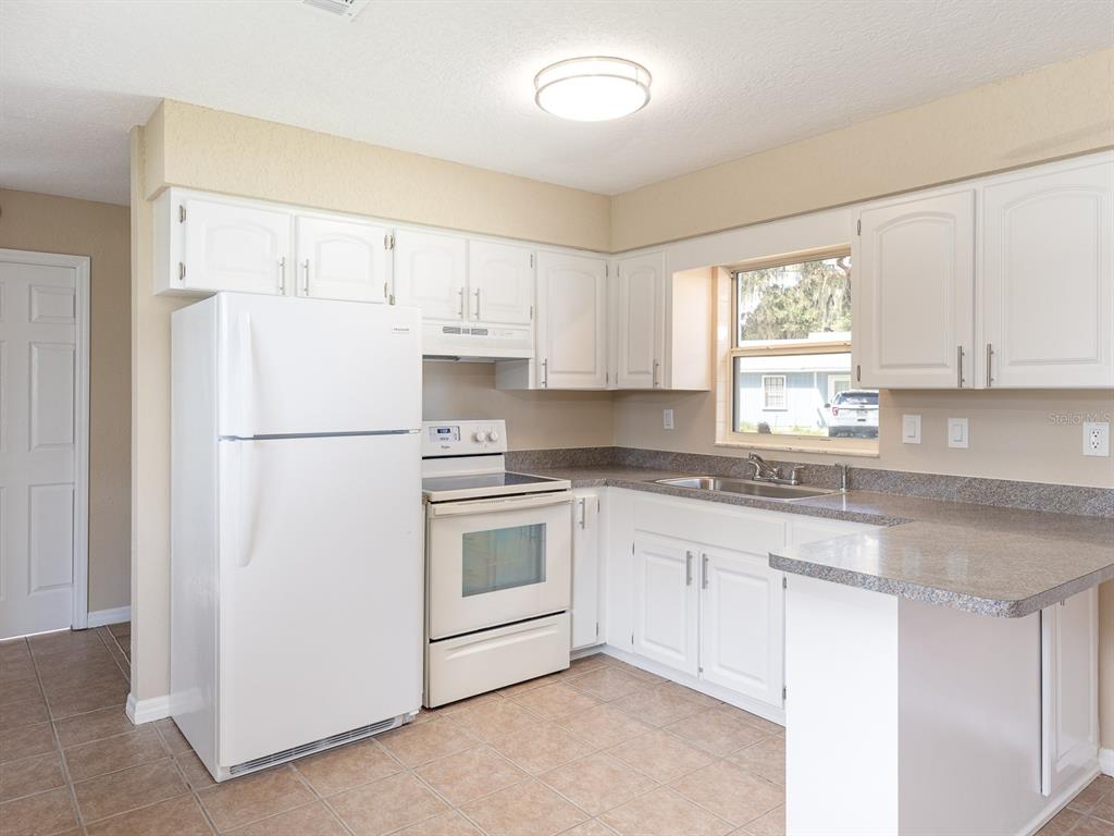 A kitchen with white cabinets, white appliances, a window, and tan tile flooring — 1314 CR 443, LAKE PANASOFFKEE, FL