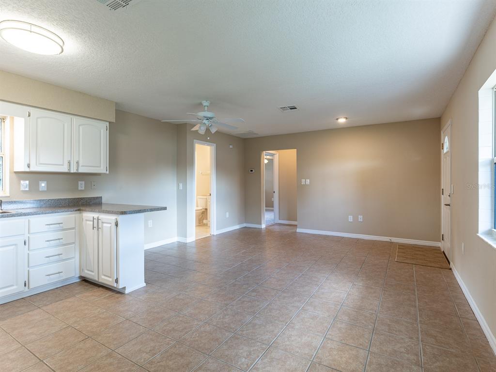 A kitchen with white cabinets and a tile floor opens into a living area — 1314 CR 443, LAKE PANASOFFKEE, FL