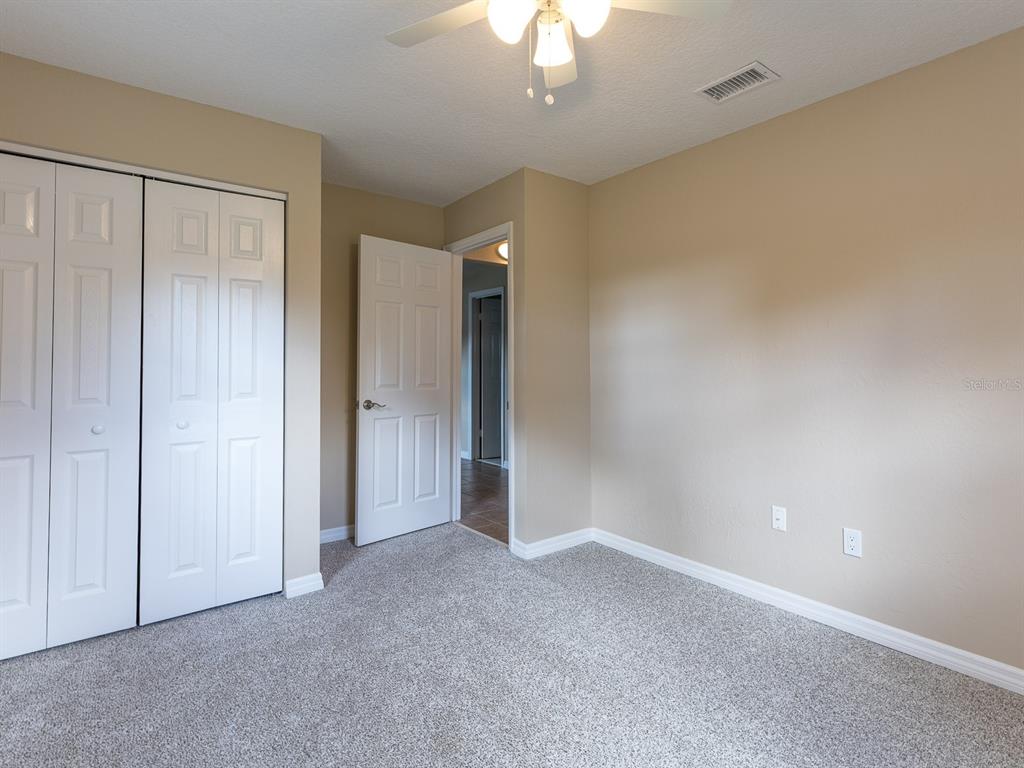 A bedroom with beige walls, gray carpet, a white closet, and a ceiling fan — 1314 CR 443, LAKE PANASOFFKEE, FL