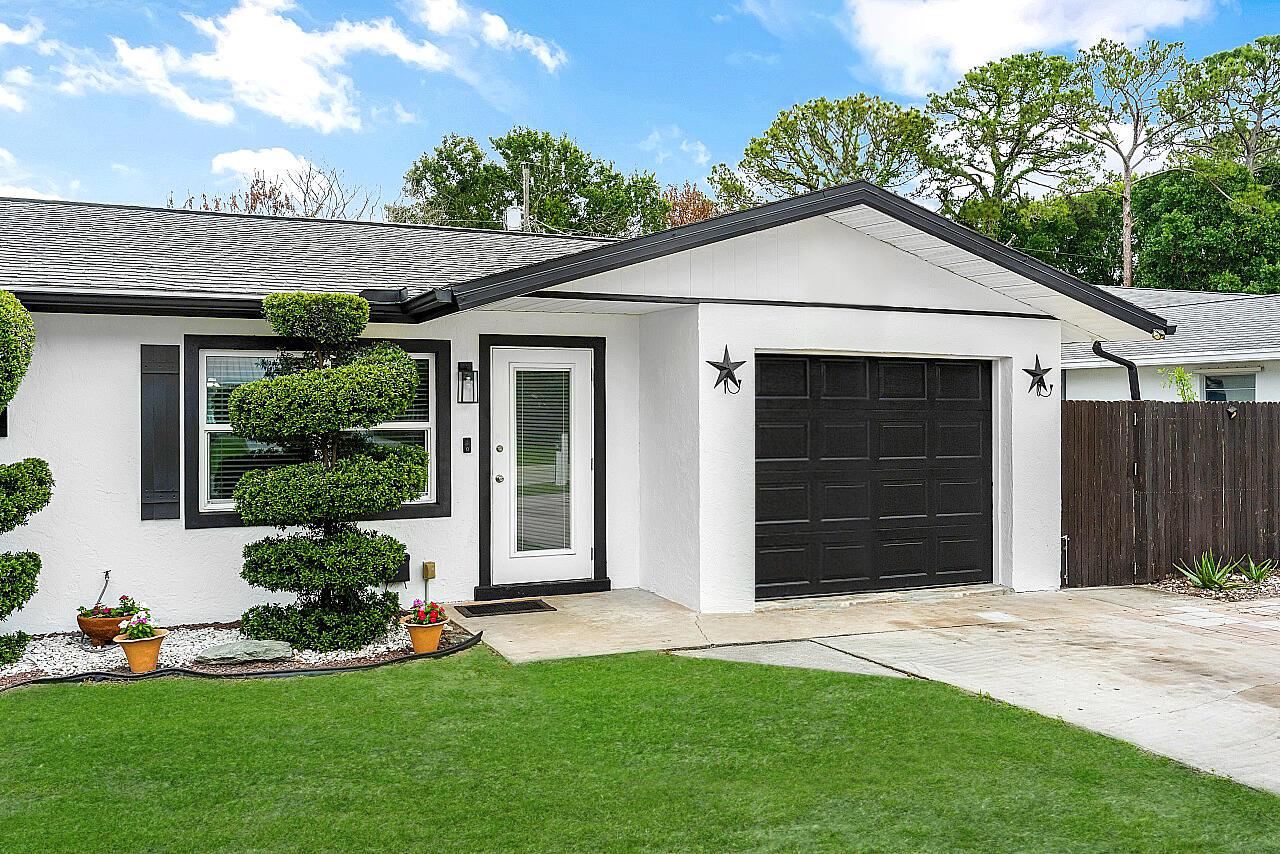 A white house exterior features a black garage door, a front door, and manicured landscaping — 266 20th Avenue, Vero Beach FL 32962, VERO BEACH, FL