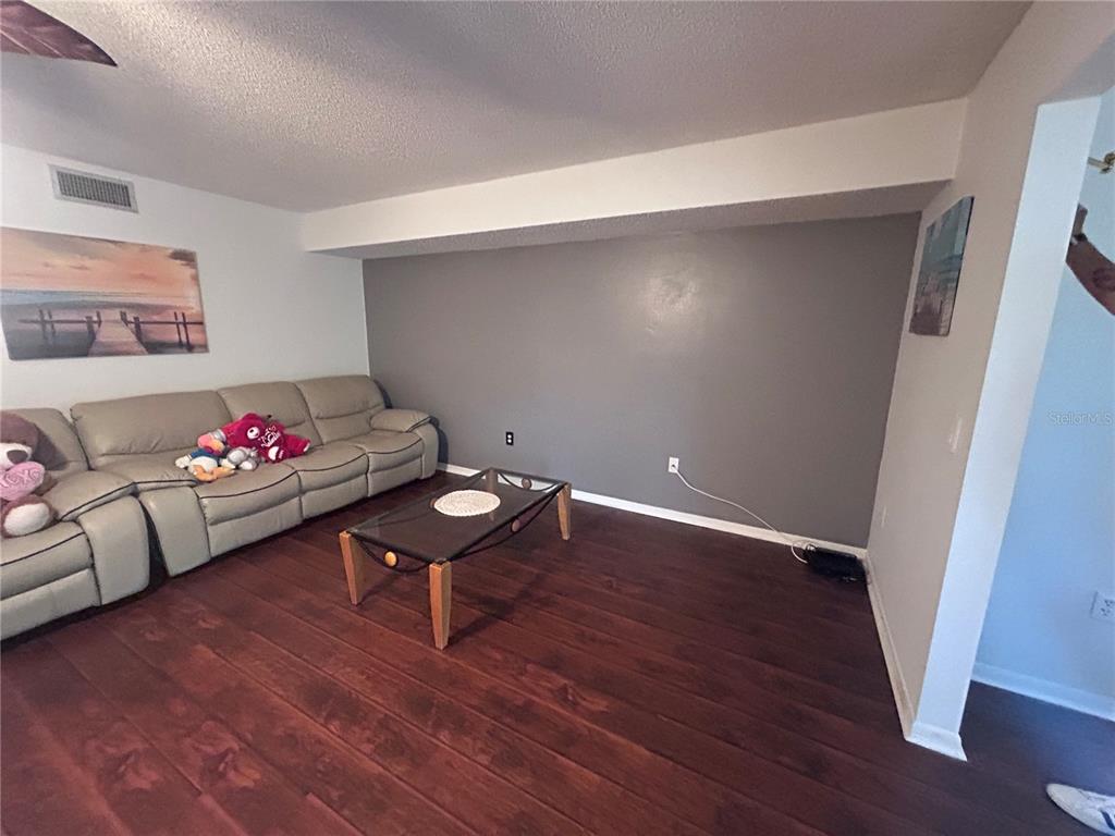 A living room features a beige reclining sofa, a glass coffee table, and dark wood flooring — 150 EL DORADO UNIT 208, WINTER HAVEN, FL